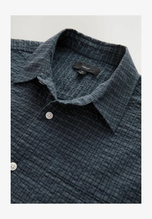Camisa de botones en azul oscuro con un patrón texturizado de cuadros, que presenta un cuello y botones blancos. Etiqueta de la marca visible en la zona del cuello.