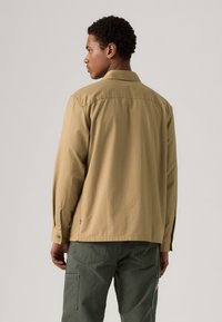 Khaki overhemd met een brede kraag, lange mouwen en knoopmanchetten, gecombineerd met groene cargobroek met opgestikte zakken en lussen.