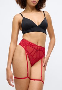Bralette noire avec un décolleté plongeant associé à un ensemble de lingerie rouge transparent avec des accents en dentelle et des attaches de jarretelles ajustables.