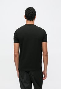 Camiseta negra de manga corta con cuello redondo, hecha de algodón. Presenta una textura suave y un diseño ajustado. Vista trasera sin detalles adicionales.