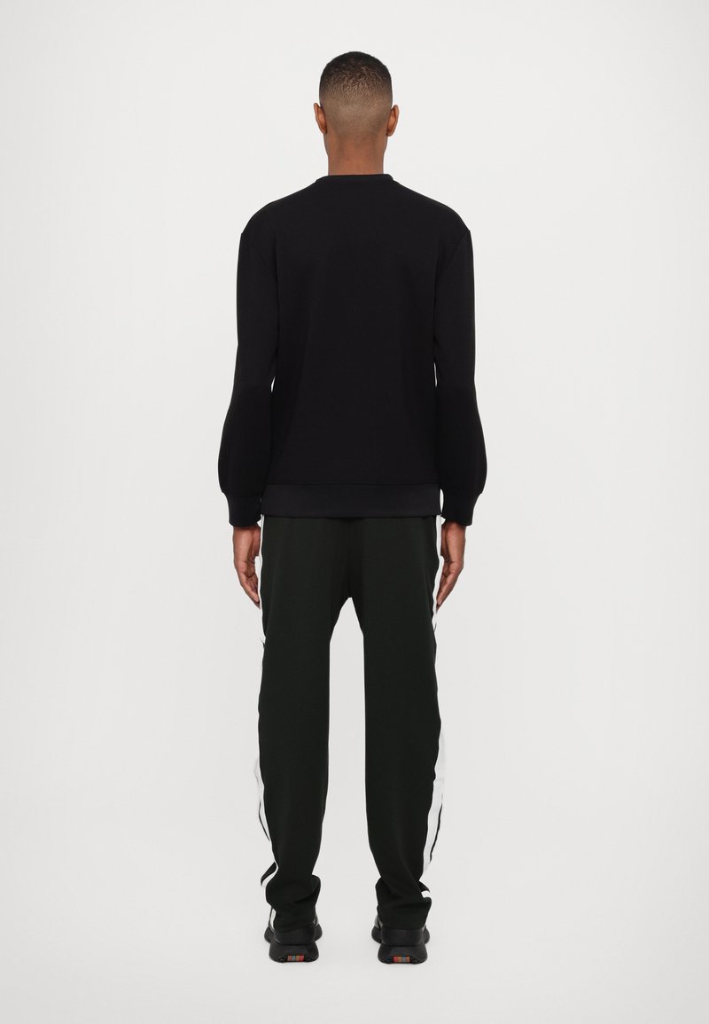 Schwarzes Sweatshirt mit Rundhalsausschnitt und Rippbündchen, kombiniert mit dunkelgrünen Jogginghosen mit weißen Seitenstreifen. Einfaches Design, moderne Passform.