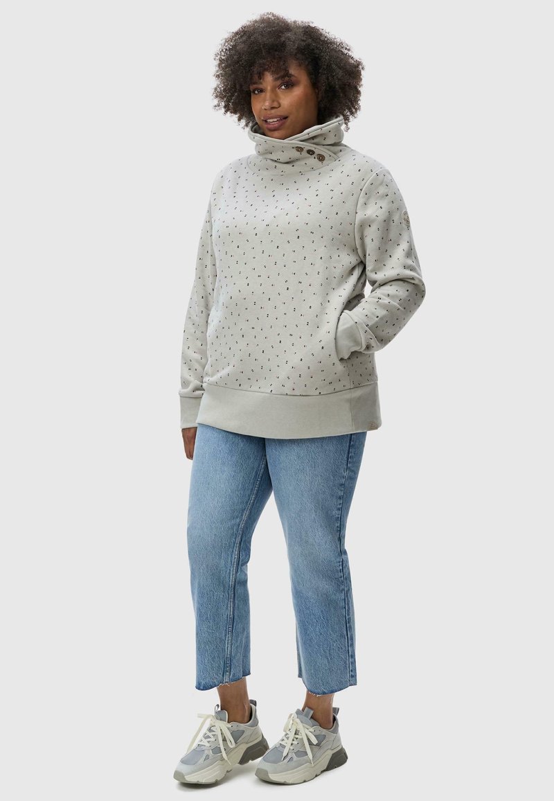 Light grey sweatshirt with a high collar, patterned with small multicolored dots, paired with blue cropped jeans and grey sneakers.