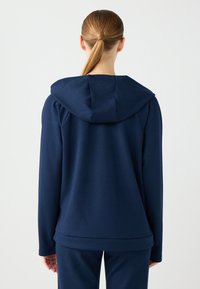 Navyblaue Kapuzenjacke aus weichem Stoff mit lockerer Passform. Verfügt über lange Ärmel und einen abgerundeten Saum. Die Rückansicht zeigt keine Logos.
