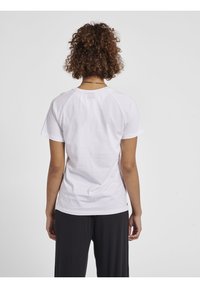 Hvid bomulds t-shirt med korte raglanærmer, en buet kant og minimale sømdetaljer, båret med sorte bukser, set fra ryggen.