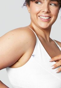 Reggiseno bianco a coste con spalline regolabili. Presenta un'etichetta di lato e una texture liscia, evidenziando una vestibilità aderente intorno alle spalle.