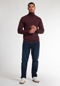 Un pull col roulé bourgogne associé à un jean bleu foncé et des baskets blanches. Le tissu semble lisse avec une coupe ajustée.
