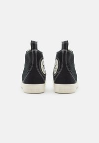 Zwarte hoge sneakers van canvas met witte rubberen zolen, contrasterende witte stiksels en een ronde logopatch aan de achterkant.