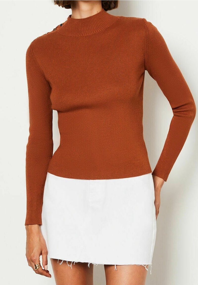 Ribbed, long-sleeve top in burnt orange with a high neck and button detail at the shoulder; paired with a white denim mini skirt.