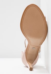 Chaussure à talon haut en suède rose clair avec un bout pointu et un talon fin. Présente une semelle en tan texturée avec de légères rainures.