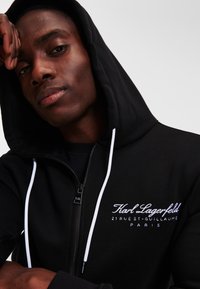 Zwarte zip-up hoodie met witte trekkoorden en geborduurd "Karl Lagerfeld" logo. Gladde stof met een relaxte pasvorm en een voormezipper.