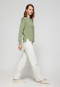 Ljust grönt stickat tröja ihop med vita vida byxor och beige sneakers. Outfitten har en avslappnad passform och en enkel design.