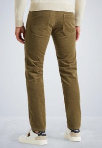 Pantaloni in corduroy khaki, slim fit, con due tasche posteriori e una texture sottile. Abbinati a sneakers bianche con il marchio sul tallone.