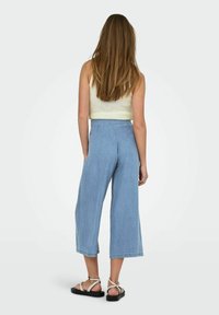 Culottes de mezclilla azul claro con cintura alta, piernas anchas y dobladillo sin rematar, combinados con un top de punto croptop beige y sandalias marrones con tiras.