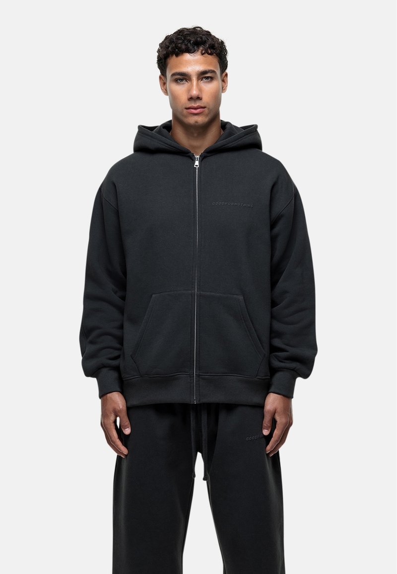 Felpa nera con zip realizzata in un tessuto a trama liscia. Presenta un cappuccio, tasche a marsupio e un branding discreto sul petto.