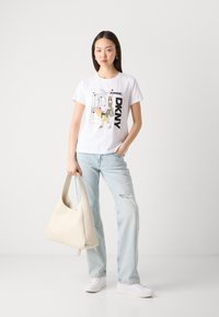 Balta trumpa rankovėmis marškinėliai su grafiniu spausdiniu ir "DKNY" tekstu, derinami su šviesiai mėlynomis suplėšytomis džinsais ir kremine spalvos rankine.