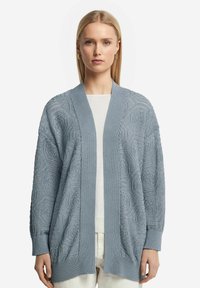 Ljust blå, stickad cardigan i strukturerad garn, med öppen front, vida ärmar och ribbade mudd. Sexkantigt mönsterdetalj.