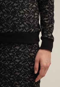 Maglione nero a maglia con un motivo testurizzato e fili argentati, rifinito con un orlo e polsini a costine neri, indossato con una gonna coordinata.