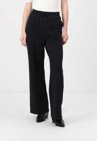 Schwarze weite Hose aus weichem Stoff, mit einem elastischen Taillenbund und einem Kordelzug sowie einer glatten Textur.