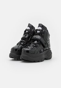 Black patent leather high-top sneakers with textured black rubber sole, laces, and adjustable straps; features logo on tongue and side.