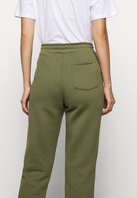 Olivgrüne Sweatpants mit lockerer Passform, elastischem Bund und einer einzelnen Gesäßtasche. Weicher Stoff und simples Design.