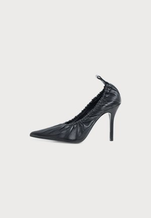 Escarpin noir en cuir à bout pointu et à talon aiguille, avec des détails froncés et une boucle au talon, sur un fond uni.