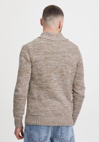 Striktrøje i en lys brun mélange med høj krave, ribbede mansjetter og kant. Har et struktureret stof med en afslappet pasform.