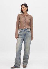 Brun ribbad cardigan med knäppning, hög halsringning och texturerad detalj, kombinerad med ljusblå vida jeans och grå spetsiga skor.