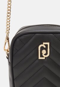 Czarna pikowana torebka skórzana z wzorem w zygzak. Posiada złotą łańcuszkową rączkę oraz złoty emblemat z przodu, dodając kontrastowy akcent.