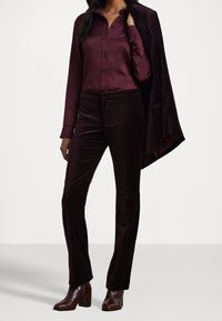 Burgunderfarbendes Hemd mit langen Ärmeln, kombiniert mit passenden Samthose und braunen Absatzstiefeln, zeichnet sich durch eine glatte Textur und eine maßgeschneiderte Passform aus.