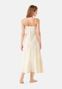 Vestido midi de seda sin mangas en crema claro con un sutil patrón floral, que presenta tirantes ajustables y una textura fluida y suave.