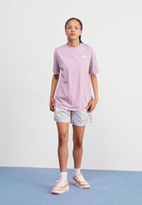 Hellblaues T-Shirt mit kurzen Ärmeln und Logo, kombiniert mit gestreiften Shorts in Weiß und Blau sowie pastellfarbenen Sneakers. Einfaches Design, lässige Passform.