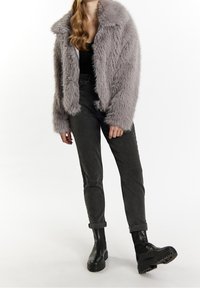 Veste en fausse fourrure gris clair avec un large col et des manches longues, associée à un pantalon gris foncé fuselé et des bottines noires.