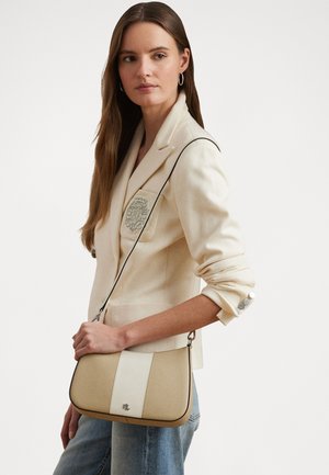 Beige keresztpántos táska krém csíkkal, sima textúrával, ezüst színű fémalkatrészekkel és logóval az elején. Világos blézer felett viselve.
