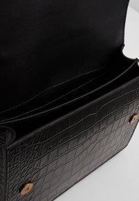 Černá kožená kabelka s krokodýlím reliéfem, hladým vnitřkem, dvěma přihrádkami a doplňky ve zlaté barvě.