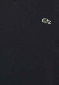 Pulover tricotat de culoare bleumarin, cu un mic logo brodat în verde reprezentând un crocodil pe partea stângă a pieptului. Design simplu cu guler rotund.