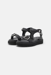Černé platformové sandály s křížovými pásky a kovovými sponami, vyrobené z hladké kůže. Obsahují strukturovanou podrážku pro lepší přilnavost.