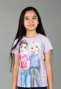 T-shirt a maniche corte di colore lilla con ragazze dei cartoni animati e nomi stampati, dettagli di abbigliamento blu e rossi, e una texture morbida e liscia.