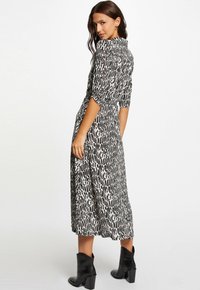 Zwart-wit gestreepte jurk, halflang met pofmouwen en een taille die aansluit, gecombineerd met zwarte enkellaarzen.