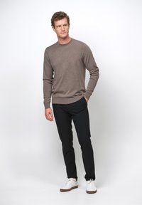 Maglione marrone a maniche lunghe con collo rotondo, abbinato a pantaloni neri e sneaker bianche. Il maglione ha una texture morbida e polsini a coste.
