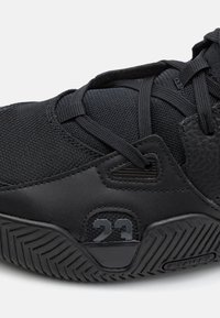 Fekete sportcipő, amely struktúrált felsőrésszel, sima bőrkiegészítőkkel és kontrasztos gumitalppal rendelkezik, zigzag mintázattal. Az oldalon a "23" szám látható.