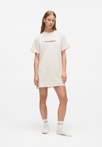 Šviesiai smėlio spalvos T-shirt suknelė trumpomis rankovėmis, apvaliu iškirpimu ir mažuoju juodu "KARL LAGERFELD" logotipu. Derinama su atitinkančiomis kojinėmis.