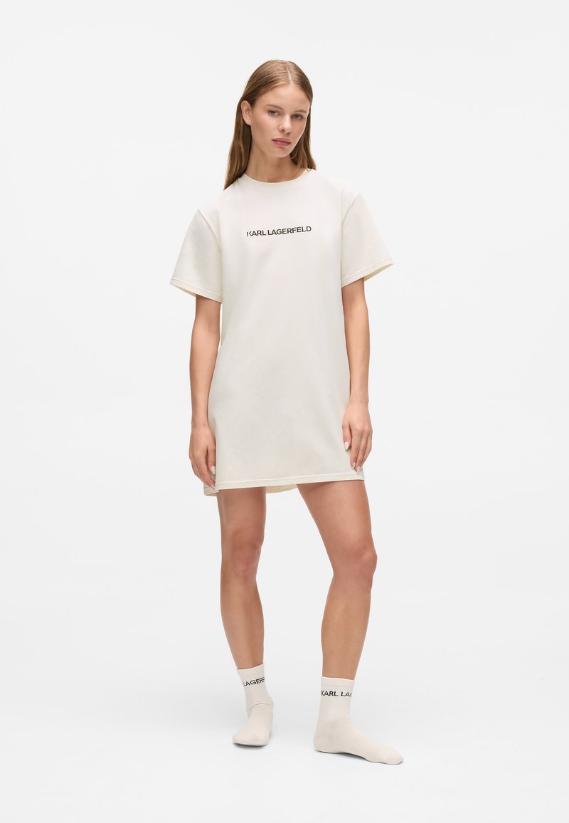 Šviesiai smėlio spalvos T-shirt suknelė trumpomis rankovėmis, apvaliu iškirpimu ir mažuoju juodu "KARL LAGERFELD" logotipu. Derinama su atitinkančiomis kojinėmis.