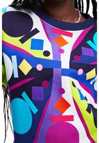 Värikäs graafinen collegepaita, jossa on erilaisia muotoja, kuten ympyröitä, kolmioita ja neliöitä, kontrastiväreissä monivärisellä taustalla.