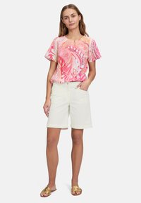 Top z krótkim rękawem w różowo-pomarańczowy abstrakcyjny wzór, zestawiony z białymi szortami. Ubranie ma luźny krój i lekki materiał.
