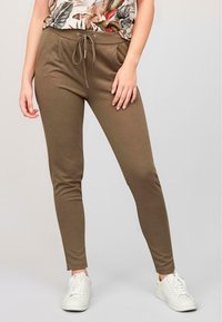Khaki slim-fit bukser med elastisk bånd i taljen, lavet af blødt stof; sat sammen med en blomstret top og hvide sneakers.