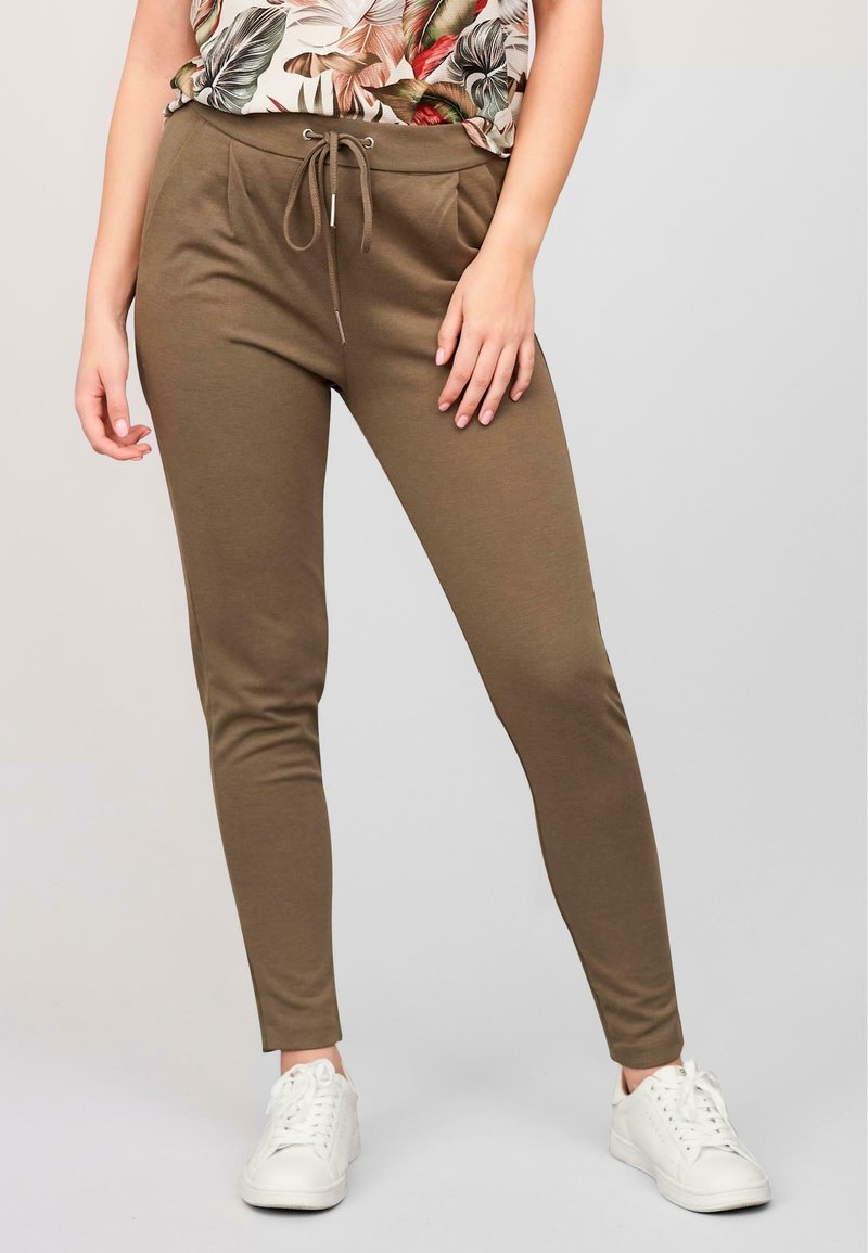 Khaki slim-fit bukser med elastisk bånd i taljen, lavet af blødt stof; sat sammen med en blomstret top og hvide sneakers.
