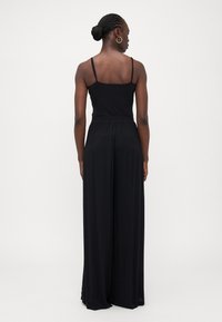 Combinaison noire sans manches avec un haut ajusté et un bas ample à jambes larges. Tissu léger, ceinture élastique et design minimaliste.