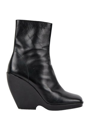 Bottine noire en cuir avec talon compensé haut et bout arrondi, affichant une texture lisse et légèrement froissée.