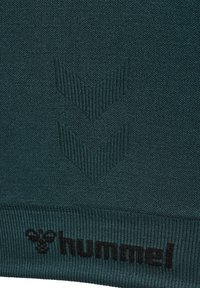 Donkergroene gebreide stof met een getextureerd pijlenpatroon en geribde boord. Zwart "hummel" logo gedrukt aan de onderkant.