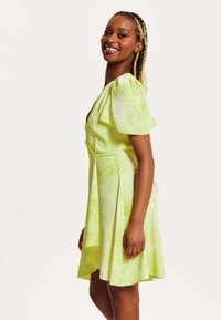 Light green tie-dye dress with short puff sleeves, V-neckline, and a flared hem. Soft fabric with a smooth texture.